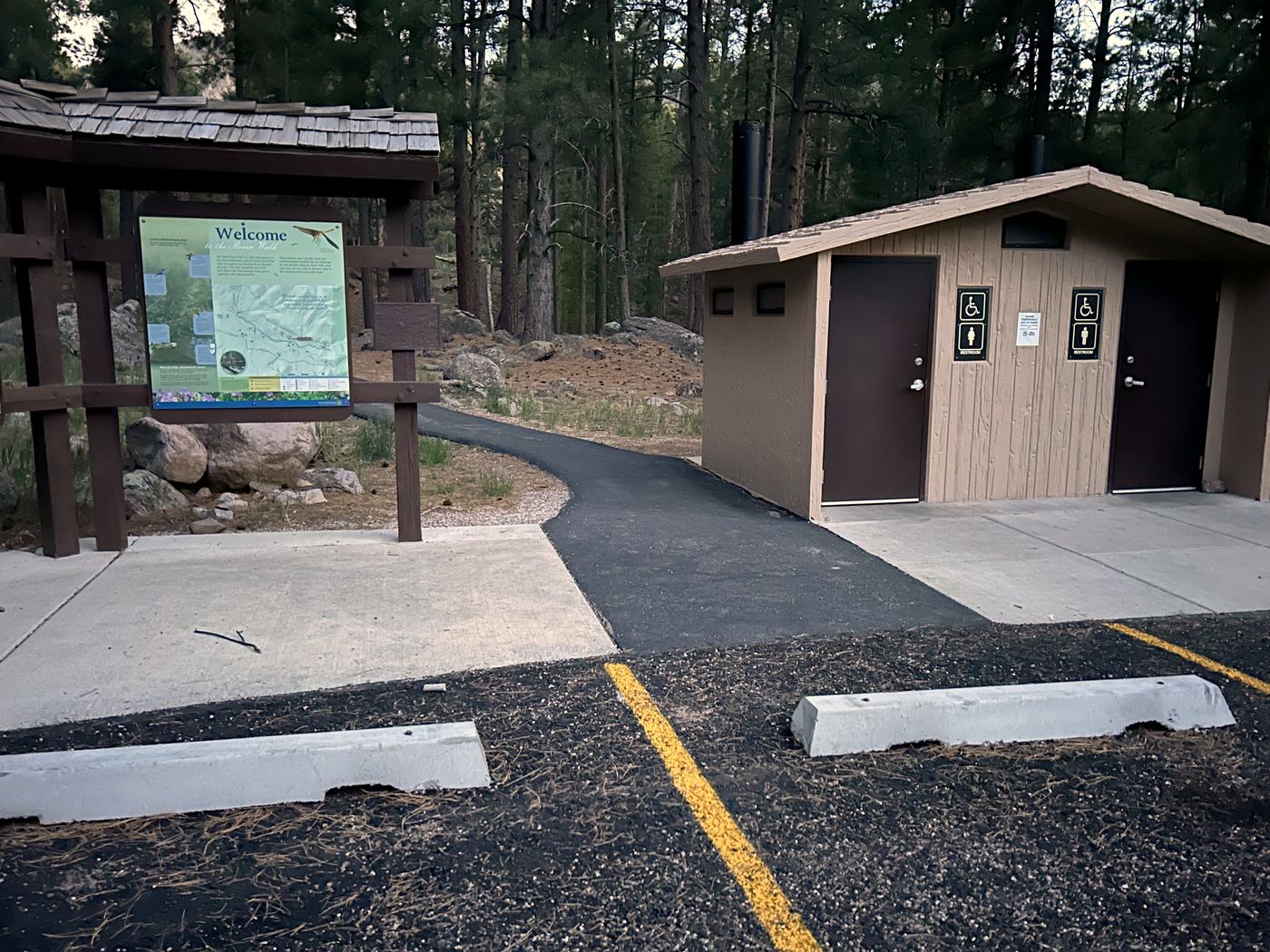 Accessible restroom building and paved trailhead path at a forest recreation site